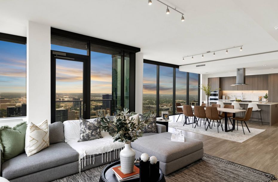 Hanover Company, Hanover Brazos Modern open-plan living and dining area with city view, large windows, comfy seating, and sleek kitchen.
