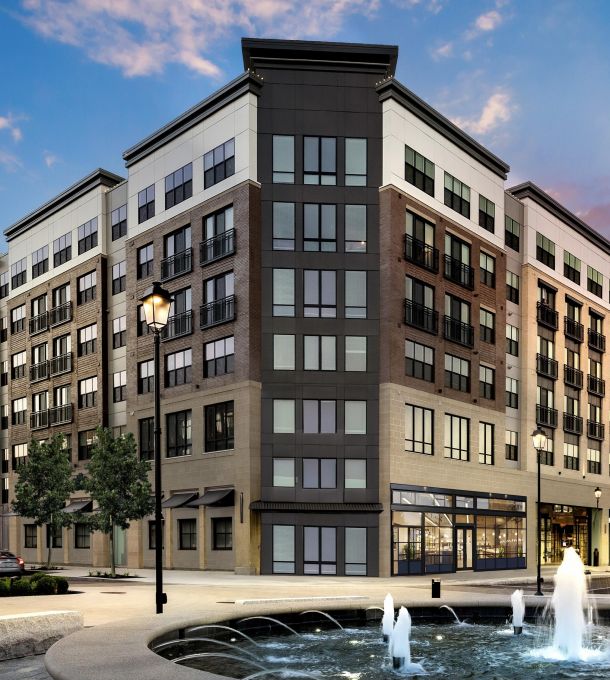 Hanover Company Modern six-story apartment building with street-level shops and a fountain in the foreground.