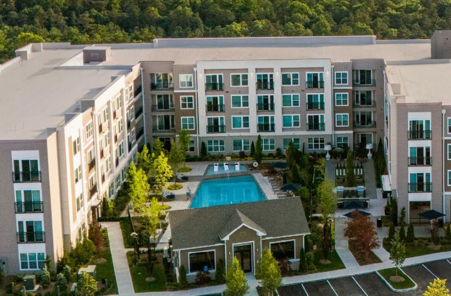 Aerial view of a modern apartment complex with a central swimming pool and surrounding trees.