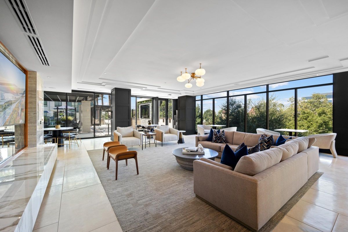 Spacious modern living room with large windows, couches, a round coffee table, and a view of trees outside.