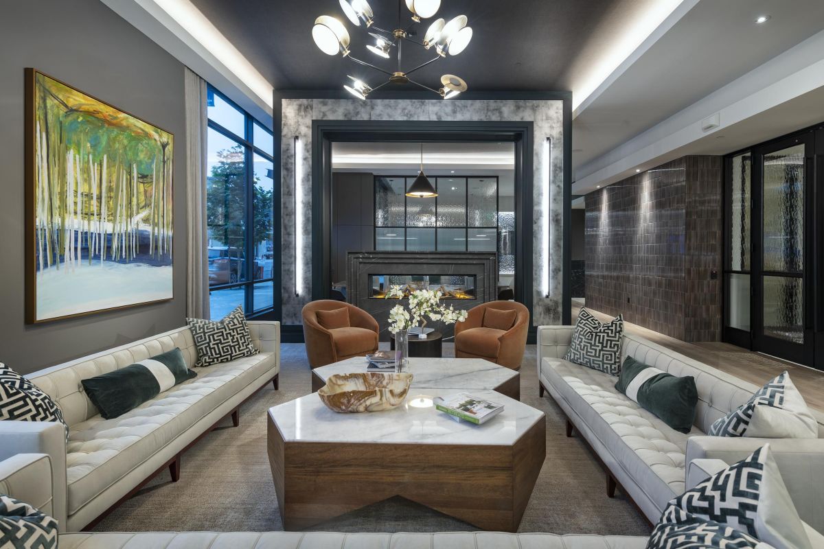 Luxurious modern living room with white sofas, hexagonal table, and abstract painting, lit by a stylish chandelier.