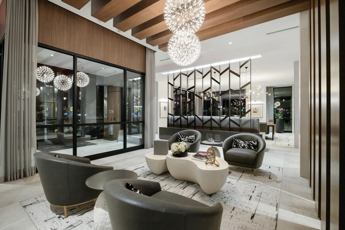 Modern lobby with stylish seating, geometric decor, and large spherical chandeliers, featuring floor-to-ceiling windows.