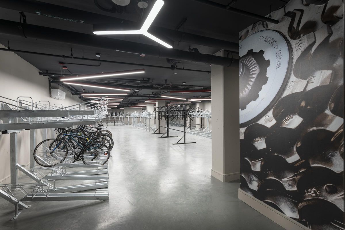 Bicycle storage room with empty racks, a few bikes, modern lighting, and a wall with gear artwork.