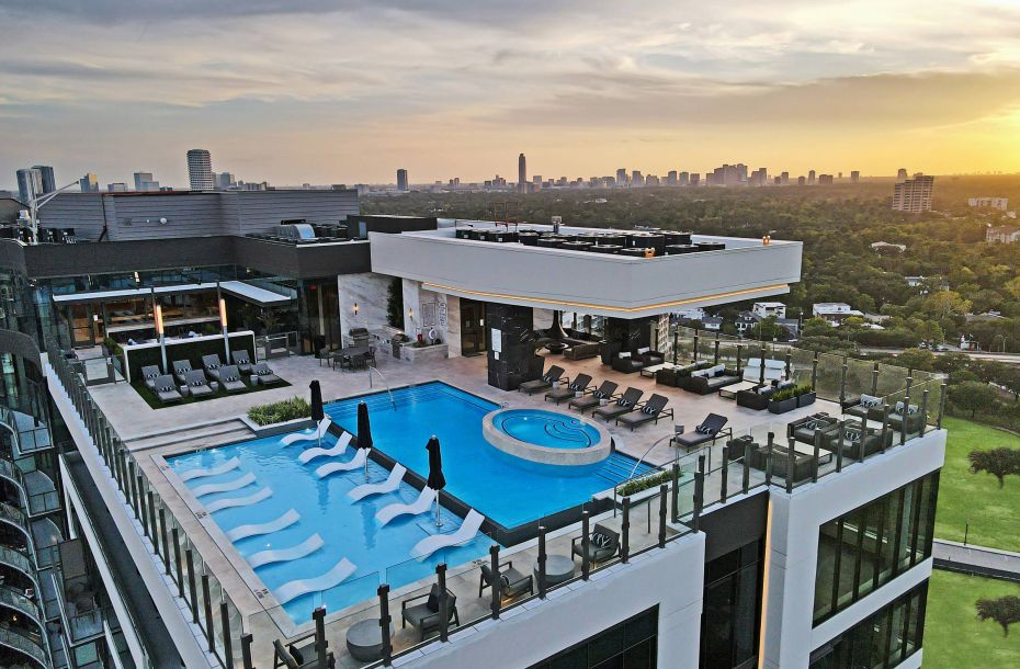 Hanover Company, Hanover Autry Park Rooftop view of a luxurious building with a pool, lounge chairs, and a city skyline at sunset.