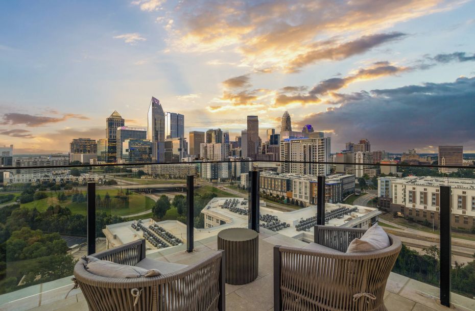 Hanover Company, Hanover Dilworth Rooftop view of a city skyline at sunset, with two chairs and a small table overlooking the scene.