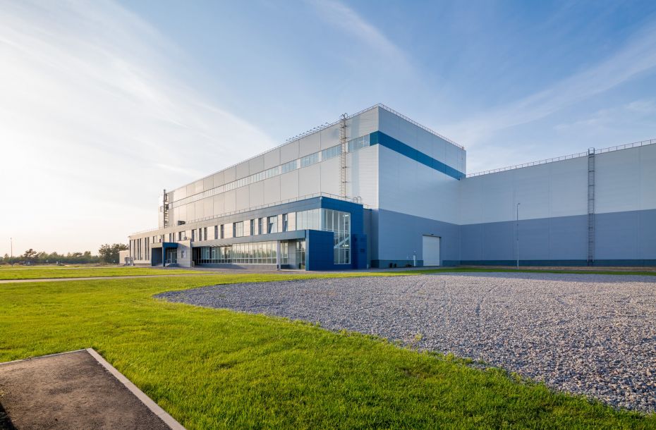 Modern, large industrial building with blue and white exterior, surrounded by grass and a gravel area.