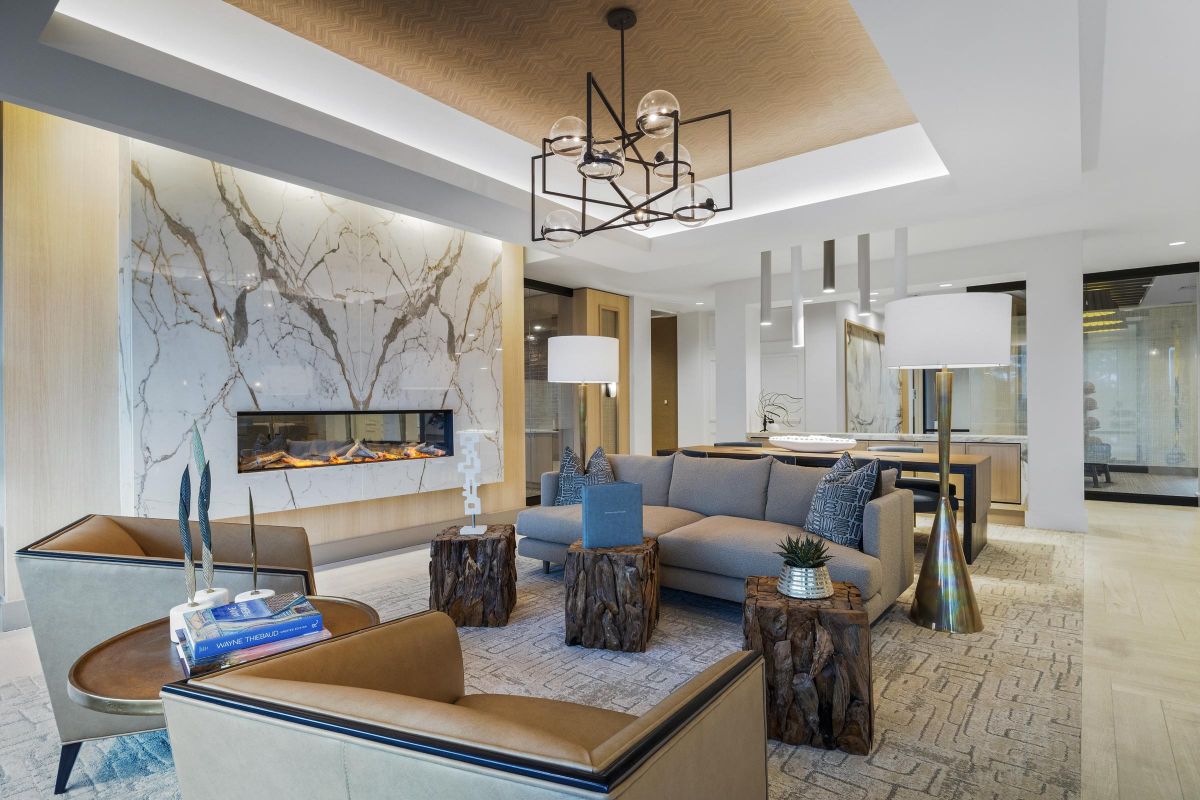 Modern living room with a beige sofa, armchairs, marble fireplace, wooden accents, and contemporary lighting.
