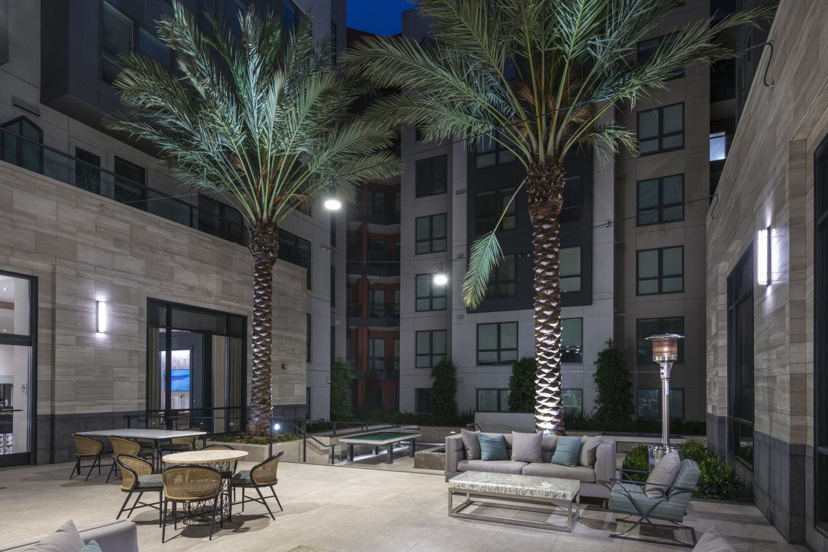 Modern courtyard at night with palm trees, seating areas, and ambient lighting.