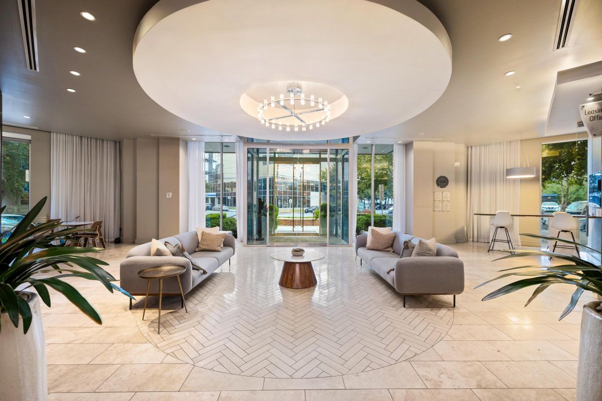 Hanover Company Modern lobby with circular ceiling light, two gray sofas, a central table, and large glass doors opening to outdoors.