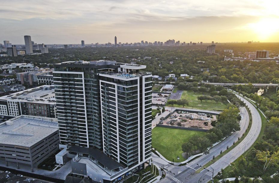 Aerial view of a tall building with a city skyline and trees at sunset.