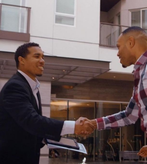 Hanover Company employee shakes hands with an apartment resident in a modern office atrium, both smiling.