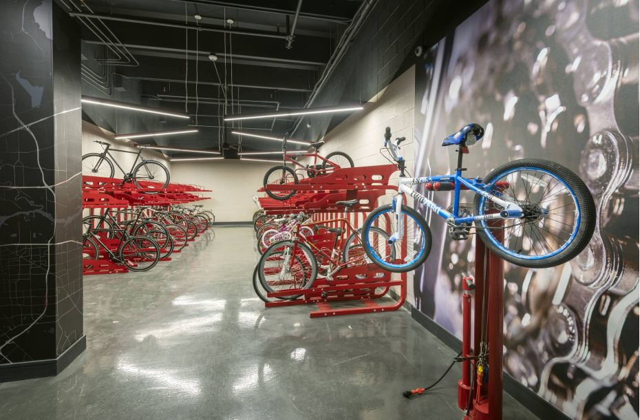 Hanover Company, Hanover BLVD Place Bike storage room with red racks and a repair station, featuring multiple bicycles and a wall mural of bike chains.