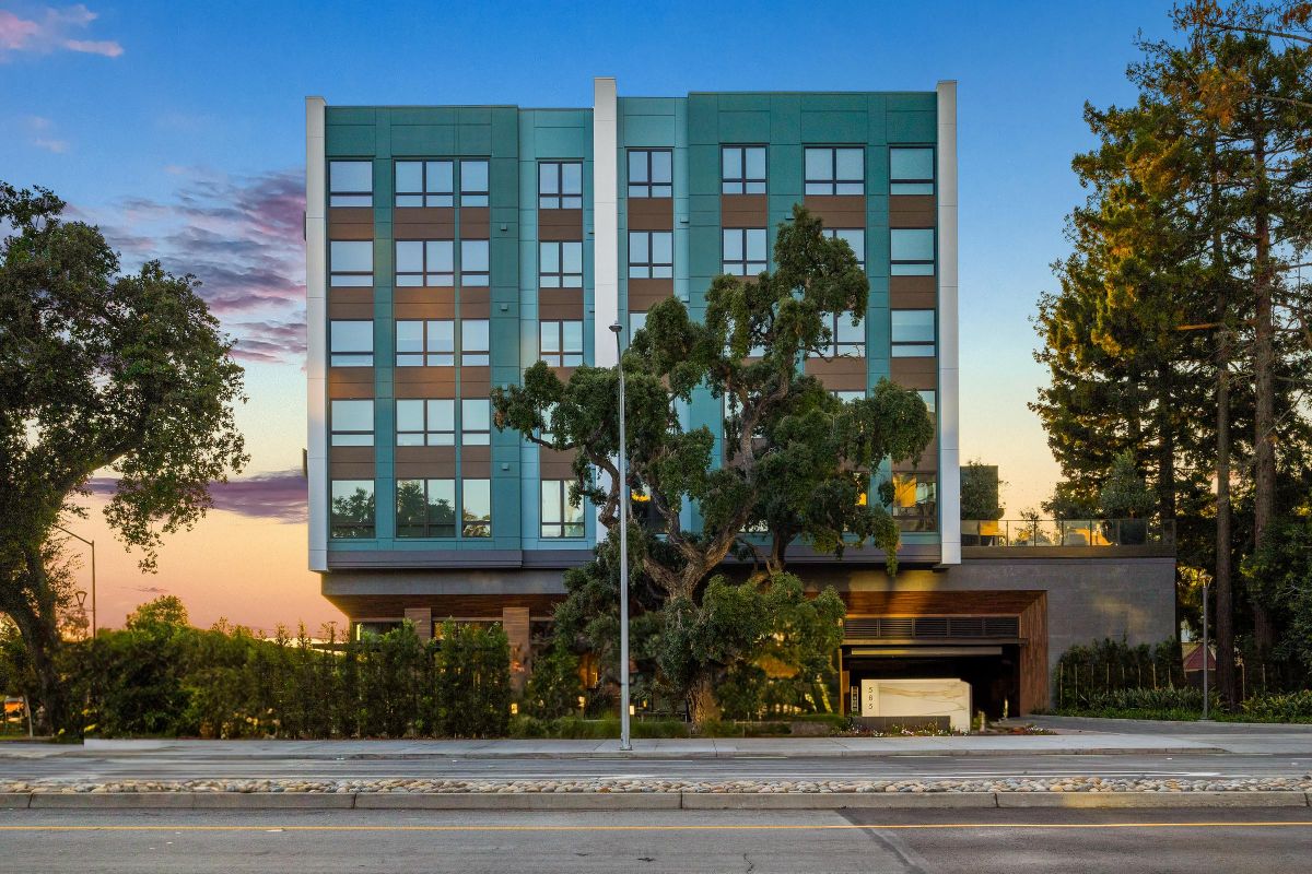 Modern building with large windows, surrounded by trees, at sunset. Road in the foreground.