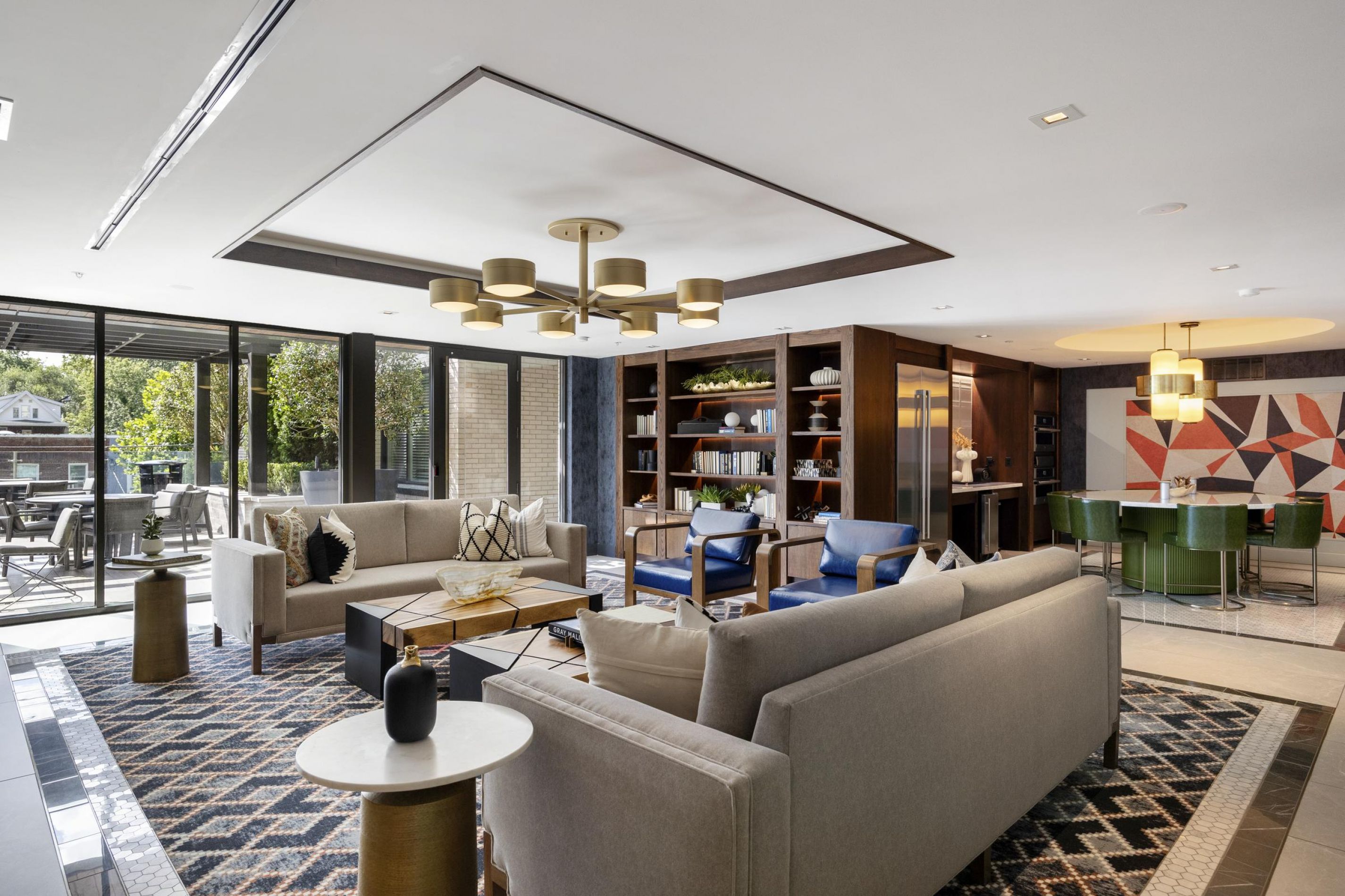 Modern living room with sofas, geometric rug, chandelier, and a view of a patio through large glass doors.