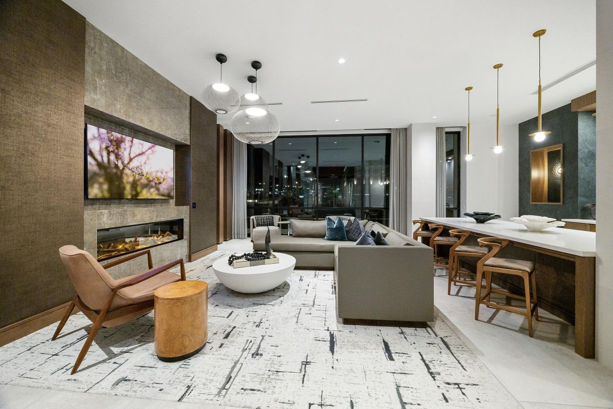 Modern living room with neutral tones, sleek furniture, and large windows overlooking a cityscape at night.