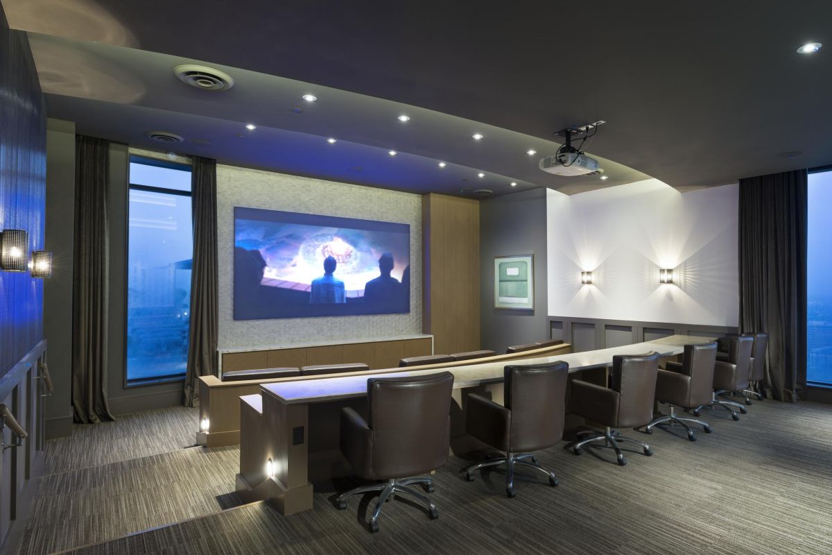 Modern conference room with leather chairs, large screen, and projector in a high-rise building with city views.