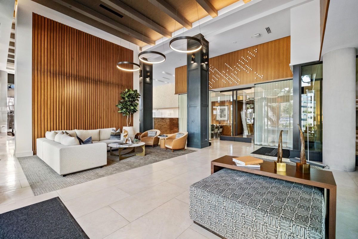 Modern hotel lobby with seating area, wooden panels, a small tree, and contemporary lighting fixtures.