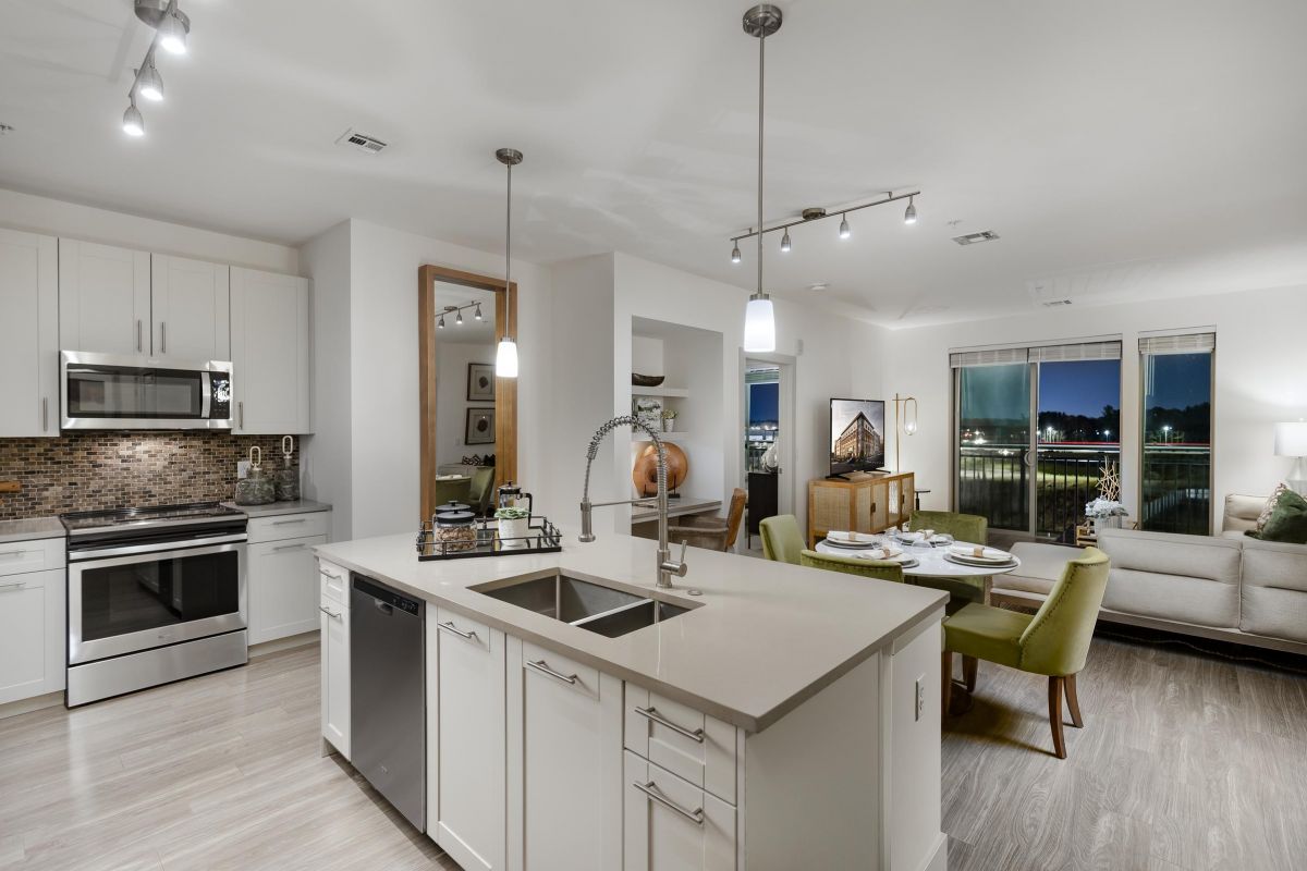 Modern open-concept kitchen and living area with dining table, sofa, and city view through large windows at night.