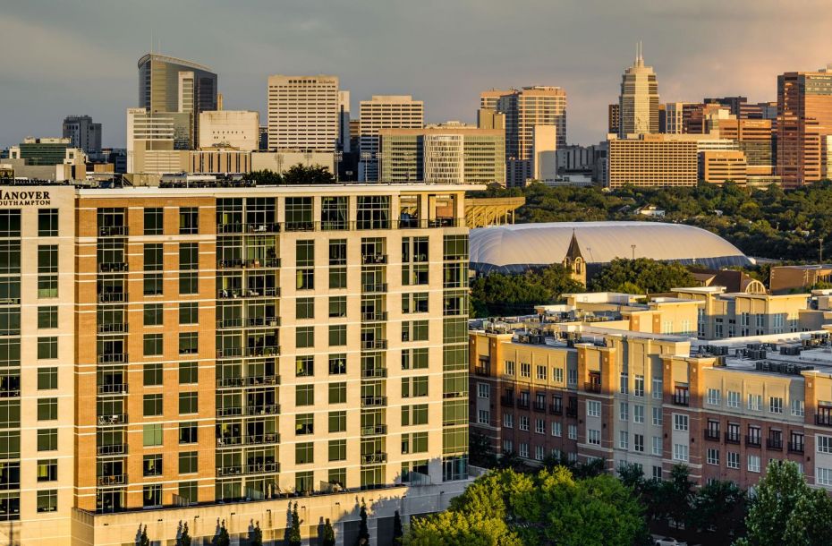 Panoramic view of an urban skyline with tall buildings and lush greenery in the foreground.