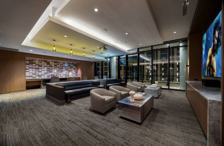 Hanover Company, Hanover Dilworth Modern lounge with sofas, armchairs, and a large TV. Glass wall reveals city lights outside.