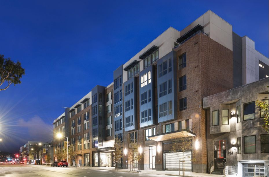 Street view of modern apartment buildings at dusk with streetlights and clear sky.