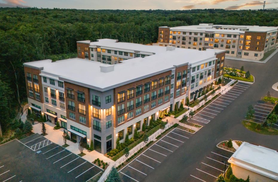 Aerial view of modern apartment buildings with lit windows and mostly empty parking lots at sunset.