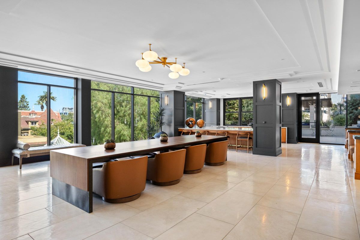 Spacious modern dining area with long wooden tables, brown chairs, and large windows offering a scenic view.
