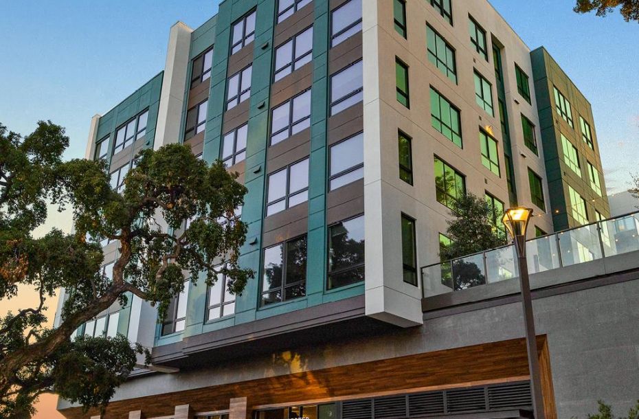 Modern mid-rise apartment building with large windows and trees in front, photographed at sunset.