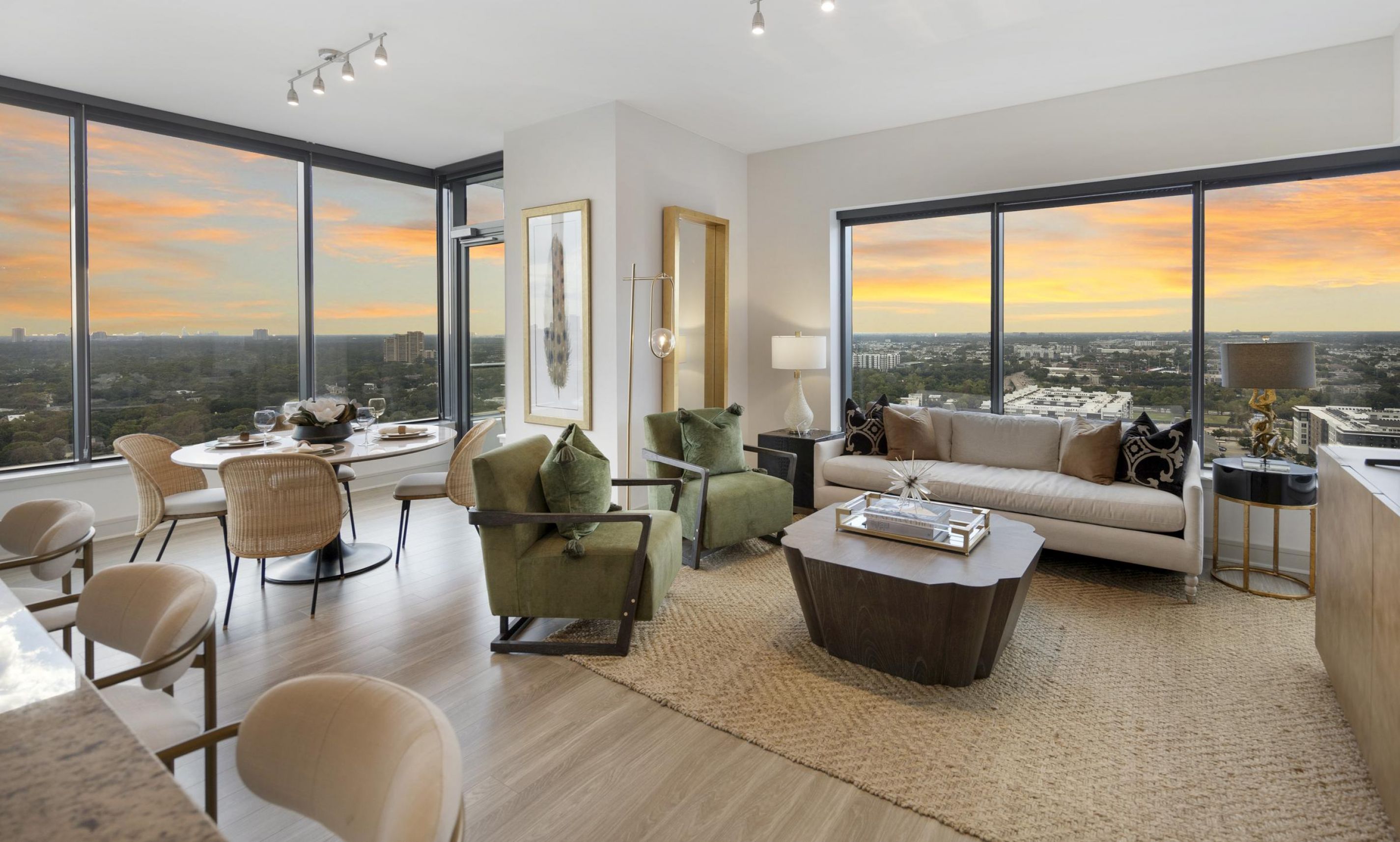 Modern living room and dining area with large windows, green chairs, and sunset city views.