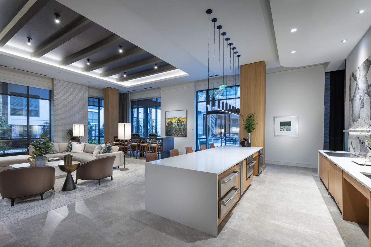 Modern living room and kitchen with sleek decor, large windows, island counter, and suspended lights.