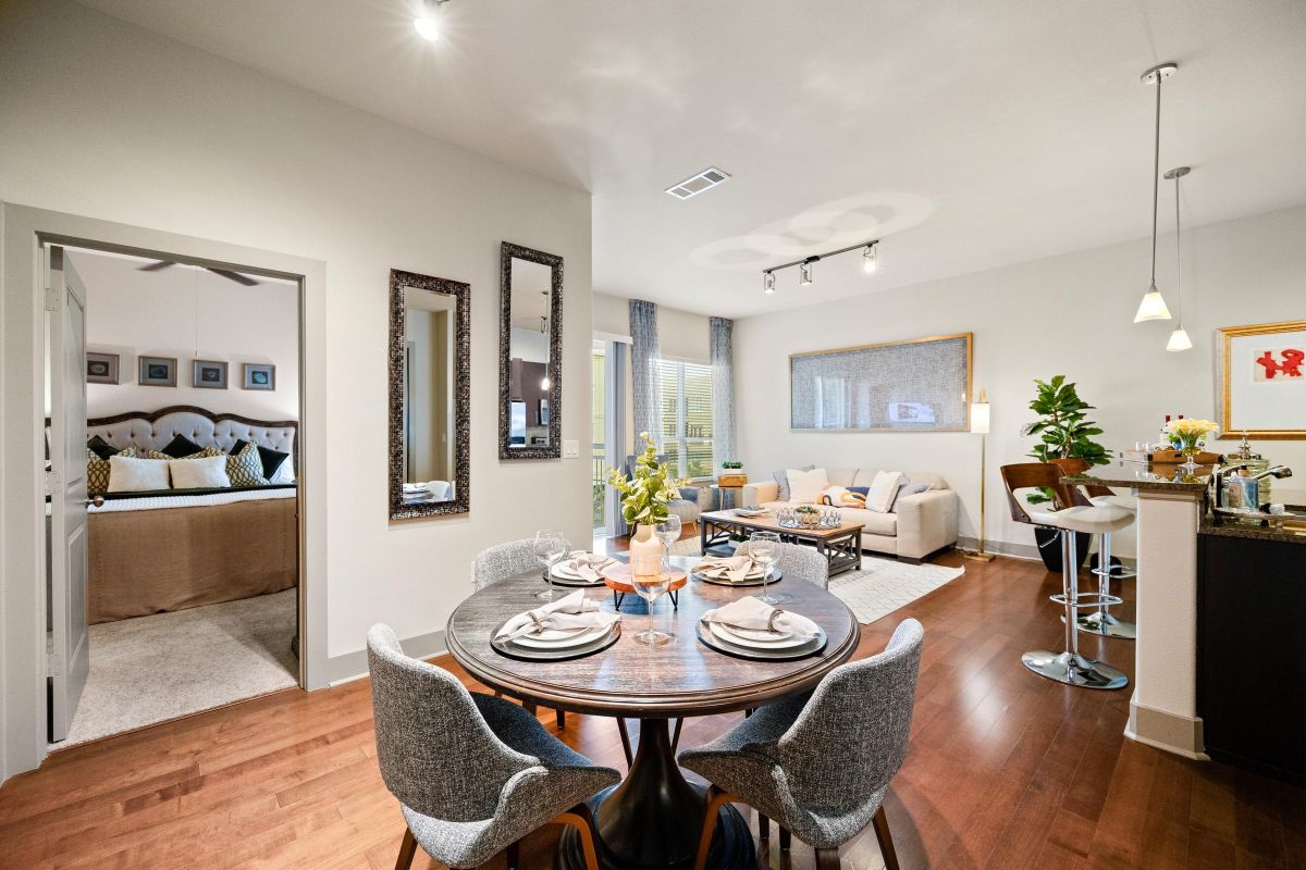 Hanover Company Modern open-plan living area with dining table, kitchen, and cozy seating. Bedroom visible through an open door.