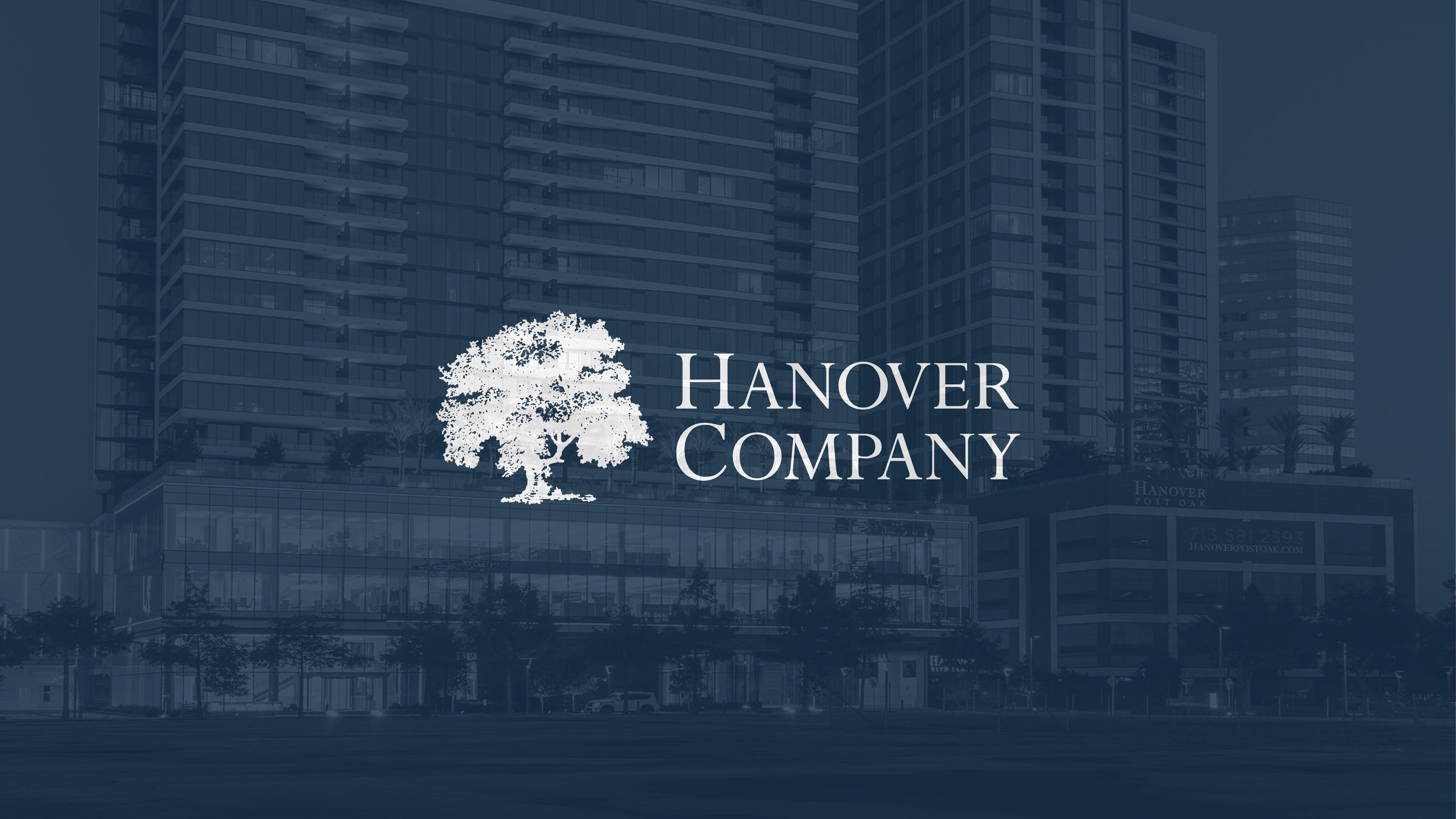 White Hanover Company logo with a tree on a green background, with buildings faintly visible behind.